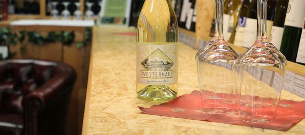 Eine Weißweinflasche mit dem Label "Schloss Westerhaus" und vier auf dem Kopf stehende Weingläser